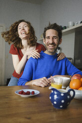 Porträt eines Mannes mit fröhlicher Frau am Tisch mit Frühstück im Zimmer - FSIF03070