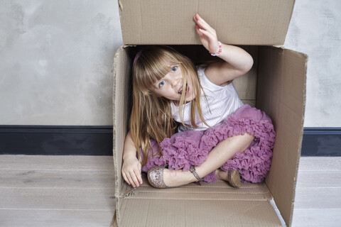 Porträt eines verspielten Mädchens, das in einem Kasten an der Wand sitzt, lizenzfreies Stockfoto