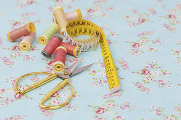 Close-up of various spools and scissors with tape measure on blue fabric - FSIF03104