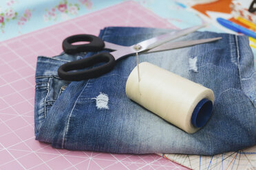 Close-up of spool and scissors with jeans on cutting mat - FSIF03105
