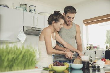 Young woman helping boyfriend to slice wholemeal bread at kitchen counter - ISF08899