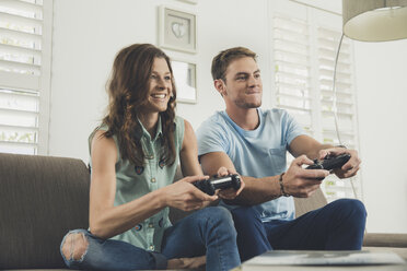 Couple on sofa using video game controller smiling - ISF08912