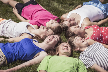 Teenage high school pupils lying head to head in circle on grass - ISF08967