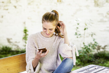 Smiling woman looking at cell phone at courtyard - FMKF05078