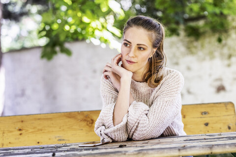 Porträt einer nachdenklichen Frau, die auf einer Bank im Innenhof sitzt, lizenzfreies Stockfoto