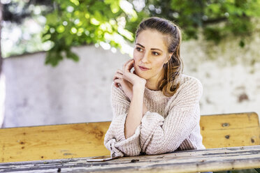 Portrait of pensive woman sitting on bench at courtyard - FMKF05087