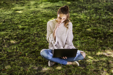 Pensive woman sitting on a meadow using laptop - FMKF05089