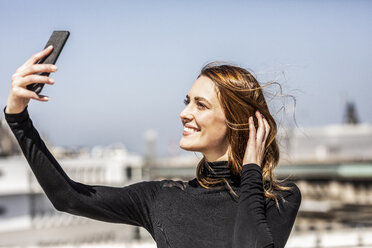 Porträt einer lächelnden Frau, die ein Selfie mit ihrem Smartphone macht - FMKF05092