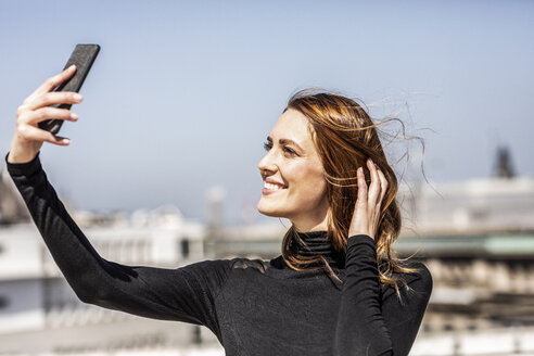 Porträt einer lächelnden Frau, die ein Selfie mit ihrem Smartphone macht - FMKF05092