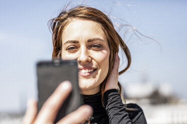 Porträt einer lächelnden Frau, die ein Selfie mit ihrem Smartphone macht - FMKF05093