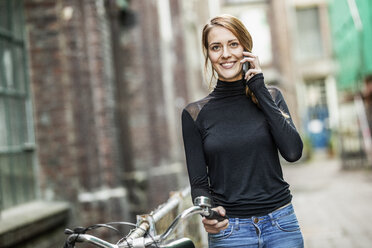 Porträt einer lächelnden Frau mit Fahrrad, die telefoniert - FMKF05103