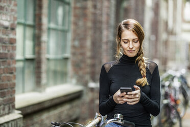 Portrait of woman with bicycle looking at cell phone - FMKF05104