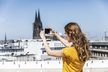 Deutschland, Köln, Frau fotografiert mit Smartphone auf Dachterrasse - FMKF05108