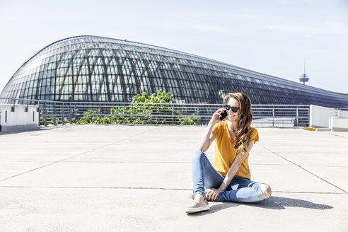 Deutschland, Köln, lächelnde Frau am Telefon sitzend auf Parkdeck - FMKF05113