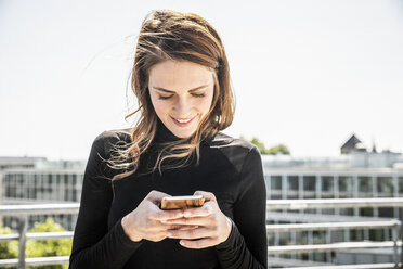 Lächelnde Frau mit SMS auf der Dachterrasse - FMKF05123