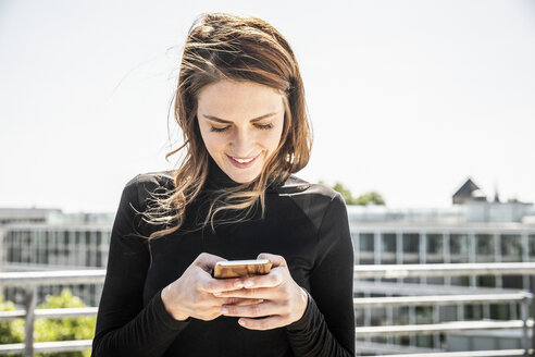 Smiling woman text messaging on roof terrace - FMKF05123