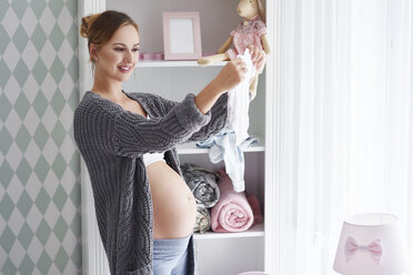 Schwangere Frau mit Babykleidung im Babyzimmer - ABIF00524