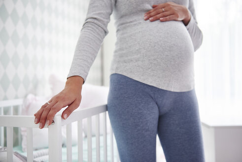 Schwangere Frau auf Babybett stehend - ABIF00526