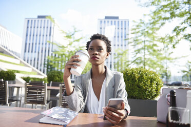 Porträt einer Geschäftsfrau mit Mobiltelefon, die in einem Straßencafé Kaffee trinkt - ABIF00539