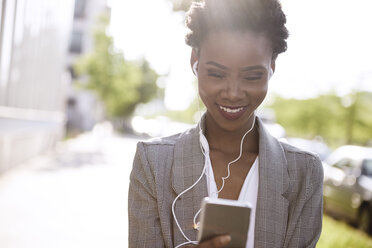 Portrait of smiling businesswoman using smartphone and earphones - ABIF00547