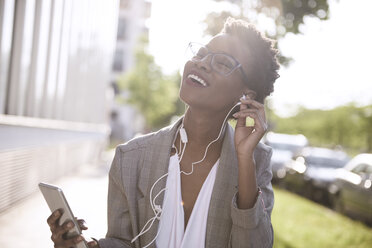 Portrait of happy businesswoman using smartphone and earphones - ABIF00548