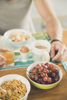 Bildausschnitt eines jungen Mannes am Frühstückstisch mit Müsli, gekochtem Ei und Weintrauben - ISF09026