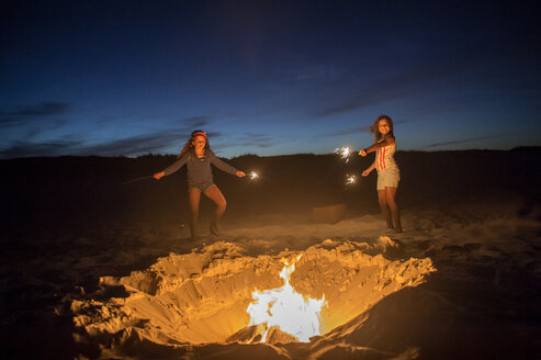 Zwei junge Mädchen halten Wunderkerzen am Strand neben einem Lagerfeuer - ISF09070