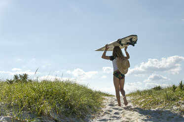 Young girl walking on sand dunes, carrying surfboard, rear view - ISF09073