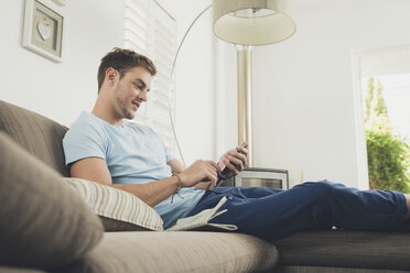 Man on sofa texting on smartphone smiling - ISF09080