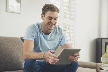 Mann auf Sofa mit digitalem Tablet lächelnd - ISF09081