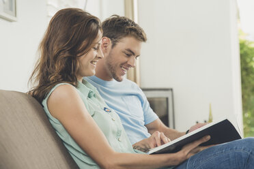 Couple on sofa looking at book smiling - ISF09082