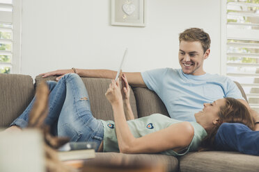 Paar entspannt sich auf dem Sofa und benutzt lächelnd ein digitales Tablet - ISF09083