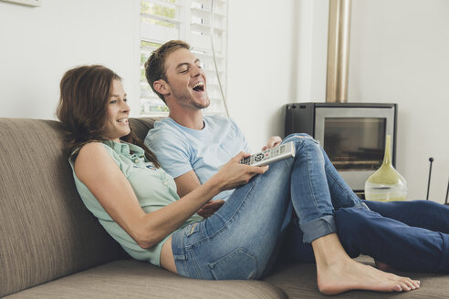 Ehepaar auf dem Sofa mit Fernbedienung lachend - ISF09084