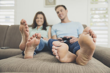 Couple barefoot on sofa using video game controller - ISF09085