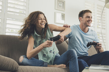 Couple on sofa using video game controller smiling - ISF09086