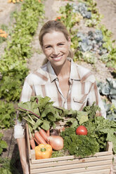 Porträt einer reifen Frau im Garten, die eine Kiste mit frischem Gemüse hält - ISF09097