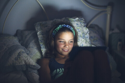 Mädchen im Bett mit digitalem Tablet lächelnd, lizenzfreies Stockfoto