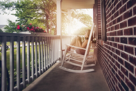 Girls on porch in rocking chair using digital tablet stock photo