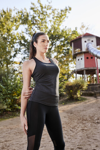 Sportliche Frau streckt Arm im Park, lizenzfreies Stockfoto