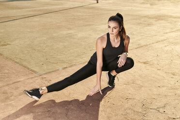 Sportive woman stretching leg on concrete floor - MMIF00123