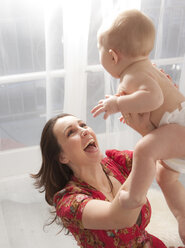 Mother lifting baby daughter in air, laughing - ISF09170