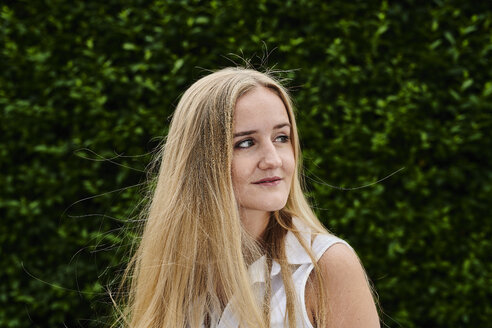 Blond young woman at a hedge looking sideways - MMIF00140