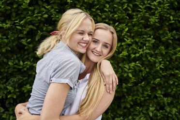 Two happy young women hugging a hedge - MMIF00141