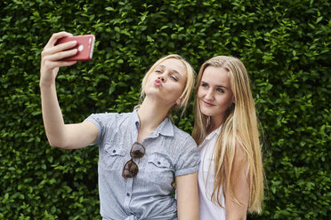 Zwei junge Frauen posieren für ein Selfie an einer Hecke - MMIF00143
