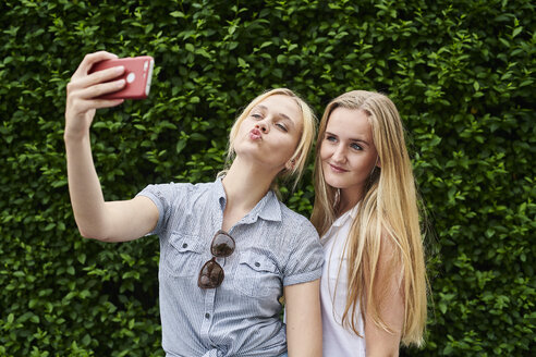 Zwei junge Frauen posieren für ein Selfie an einer Hecke - MMIF00143