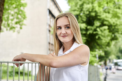 Porträt einer lächelnden blonden jungen Frau an einem Zaun - MMIF00149