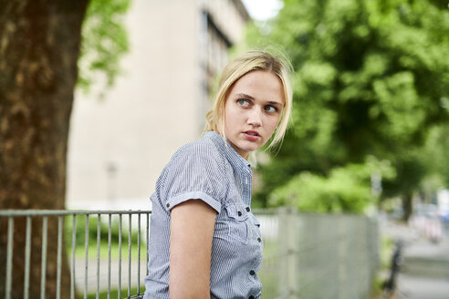 Serious blond young woman at a fence - MMIF00153