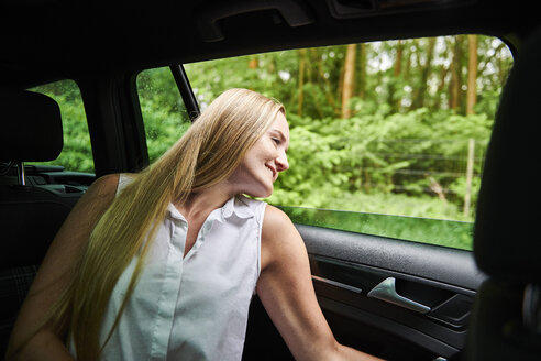 Lächelnde blonde junge Frau in einem Auto, die aus dem Fenster schaut - MMIF00156