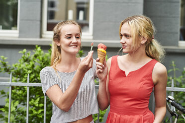 Zwei junge Frauen teilen sich eine Eiswaffel in der Stadt - MMIF00160