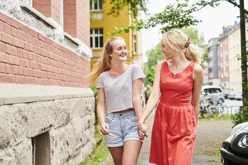 Zwei glückliche junge Frauen gehen Hand in Hand in der Stadt spazieren - MMIF00161